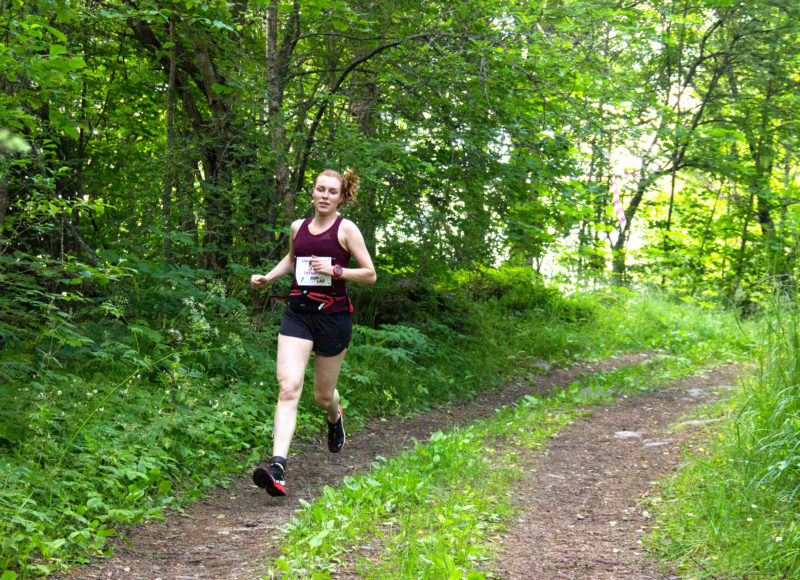 Woman running down a trail through bright green woods